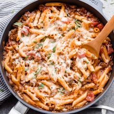 a skillet filled with pasta and sauce on top of a towel next to a wooden spoon