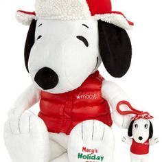 a white stuffed dog wearing a red vest and holding a small christmas ornament