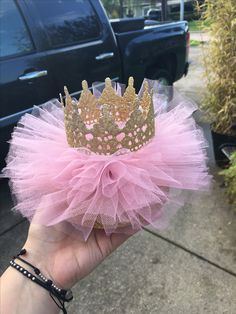 a hand holding a pink tutu with a gold crown on it's head