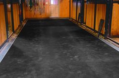 the inside of a horse barn with wooden walls and black carpeted flooring on both sides