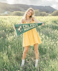 a woman in a yellow dress is holding a green and white sign that says cal poly mustangs