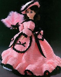 a crocheted doll is wearing a pink dress and hat with black trims