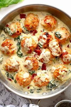 a pan filled with meatballs covered in white sauce and spinach sprinkled on top