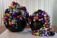 two black vases filled with colorful ornaments on top of a paper work surface next to each other