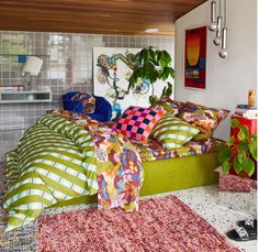 a bed with lots of pillows on top of it in a room filled with plants