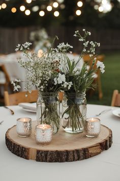 mason jars filled with flowers and lit candles are on a wooden slice at the head table