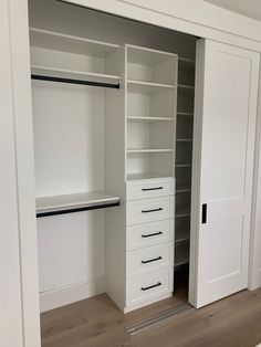 an empty walk in closet with white shelves and drawers on the door, next to a wooden floor