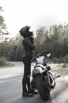 a person standing next to a motorcycle on the side of the road with trees in the background