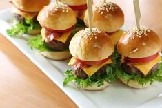 mini hamburgers with cheese and lettuce are on a white plate, ready to be eaten