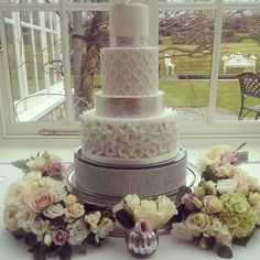 a white wedding cake with flowers on the table in front of a window and an uk seller sign