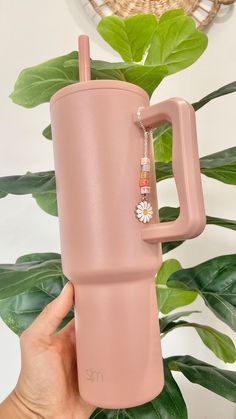 a person holding a pink travel mug with a flower charm on it