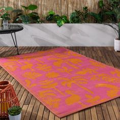 a pink and orange rug sitting on top of a wooden floor next to potted plants