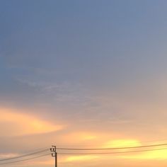 the sun is setting behind power lines and telephone poles in an empty field with no cars