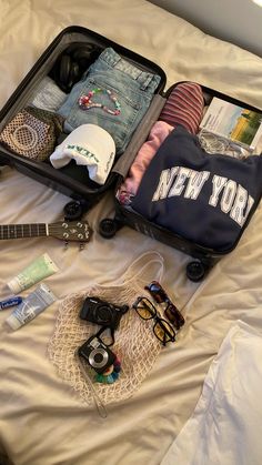 an open suitcase sitting on top of a bed filled with clothing and other items next to sunglasses