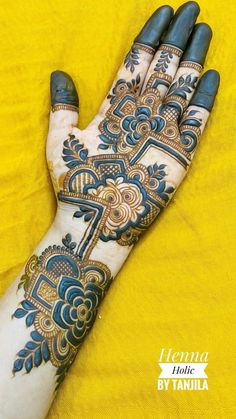 the hand is decorated with blue and gold henna designs on yellow fabric, it looks like