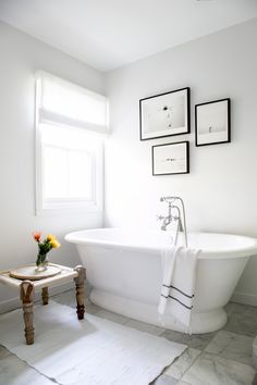 a white bath tub sitting in a bathroom next to a table with flowers on it