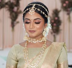 a woman wearing a gold and white bridal outfit with pearls on her necklaces