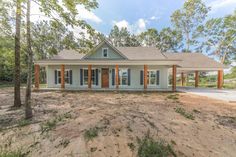 a house that is in the middle of some dirt with trees and bushes around it