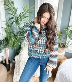 a woman standing in front of a window wearing a sweater and jeans with her hands on her hips