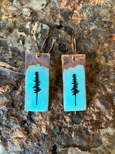 two earrings with trees on them sitting on a rock