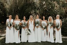 a group of women standing next to each other in front of trees and bushes holding bouquets