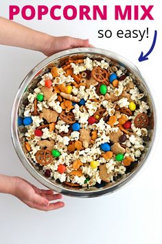 two hands holding a metal bowl filled with cereal and pretzel treats on white background