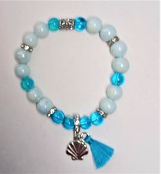 Beautiful Stretchy Beaded Bracelet with Silver Shell and Tassel Charm.  Sea Blue translucent beads and White with a hint of blue color 8mm beads, this bracelet adds elegance to your ensemble.  8mm glass beads.  Beaded Bracelet includes 11 mm silver shell charm and 12mm sea blue tassel. Handmade with love and care by Grandma B, this bracelet has great colors.  Wear every day or for special occasions.  Gift for Anniversaries, Holidays, Birthdays or any other occasion. Cute Beaded Bracelets, Charm Beaded Bracelet, Colorful Bead Bracelets, Coastal Jewelry, Stretchy Beaded Bracelet, Bracelets To Make, Bracelets Beads, Blue Beaded Bracelets, 8mm Beads