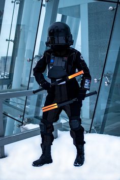 a man in a black suit and helmet holding two ski poles standing on snow covered ground