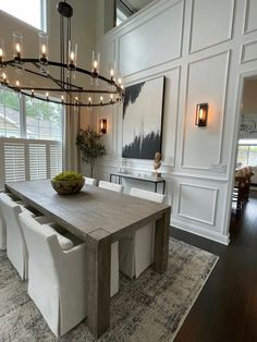 a dining room table with white chairs and a bowl of fruit on the centerpiece