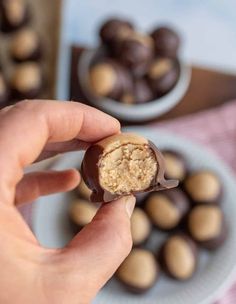 a hand holding a peanut butter ball in front of some chocolates on a plate