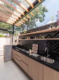 an outdoor kitchen with black counter tops and wooden shelves on the wall, along with stainless steel sinks