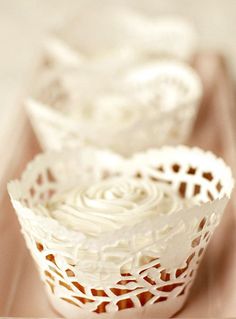 two white cupcakes sitting on top of a pink tray with lace doily