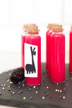 three bottles filled with raspberry jelly on top of a black tray covered in sprinkles