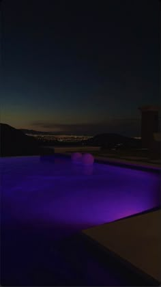 an empty swimming pool at night with the lights on and buildings in the background,