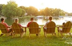 four people sitting on lawn chairs in front of a lake