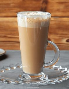 there is a cup of coffee on the glass plate with spoons next to it