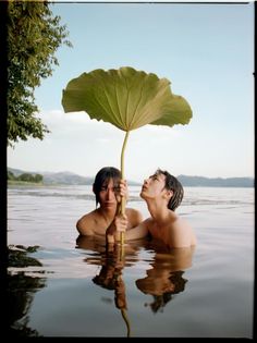 two people are in the water with a large leaf on their head and one person is holding