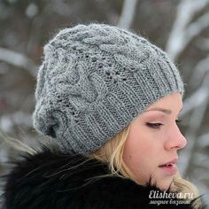 a woman wearing a gray knitted hat and black fur coat in front of snow covered trees