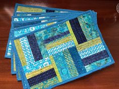 three placemats with blue and yellow designs on them sitting on a wooden table