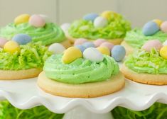 decorated cookies with green frosting and candy eggs on a white cake platter in front of grass