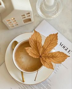 A cup of hot coffee with a fall leave on top and a Vogue paper underneath. Fall Coffee Photography, Autumn Coffee Aesthetic, Pumpkin Spice Latte Aesthetic, Fall Coffee Aesthetic, October Coffee, Earrings Photography, Pumpkin Aesthetic, Latte Aesthetic