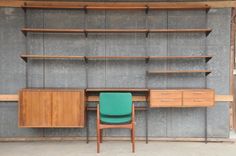 a green chair sitting in front of a wooden desk and bookcase with shelving on the wall