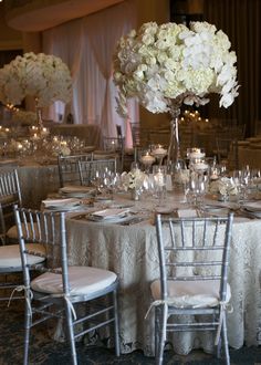 the tables are set up with white flowers and silver chairs for an elegant wedding reception