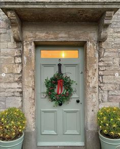 a green door with a wreath on it and two planters in front of it