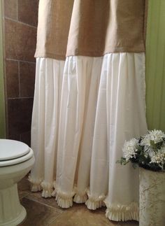 a white toilet sitting next to a shower curtain in a bathroom with brown tile flooring