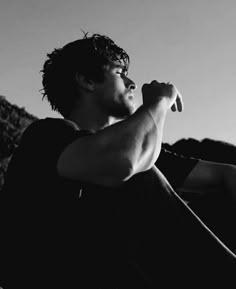 black and white photograph of a man sitting on the ground with his hand in his mouth