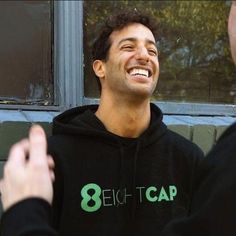 a smiling man in a black hoodie with the eight eight cap logo on it