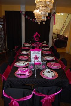 a table set up for a party with pink and black plates, napkins and place settings