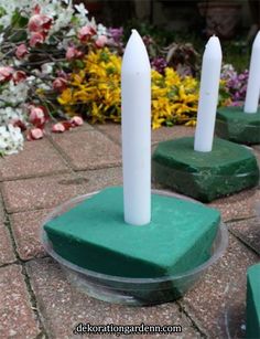 four candles sitting on top of green bases in front of flowers and bushes with white stems sticking out of them