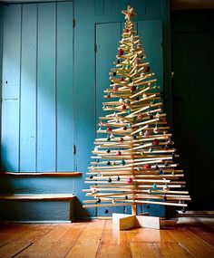 a small wooden christmas tree sitting on top of a hard wood floor next to a blue wall